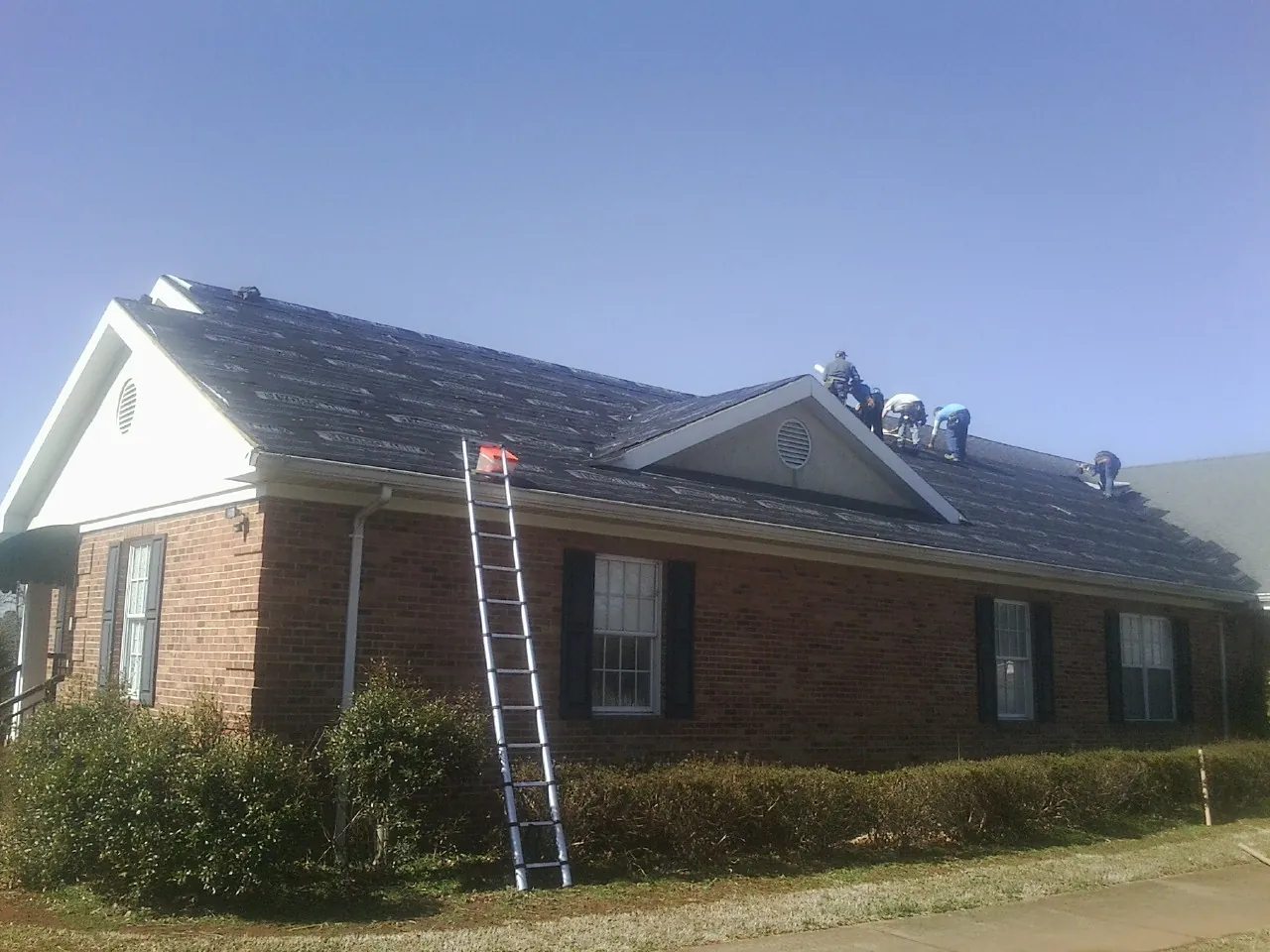 Crew tearing shingles off a brick ranch roof with a ladder set — Metal Roof Repair work by our crew in Glen Hope