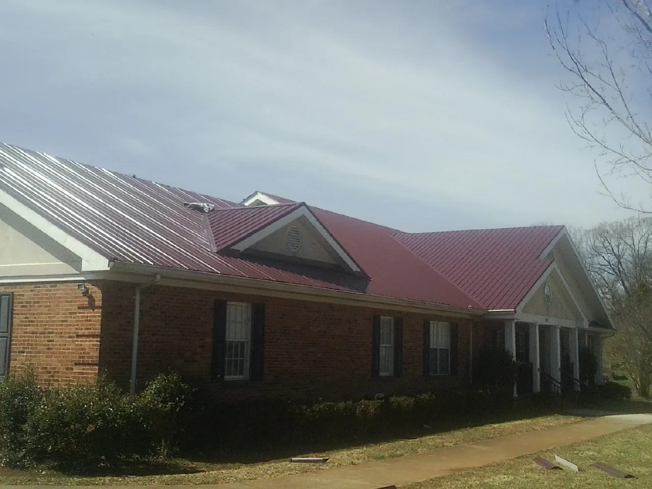 Red metal roof with gabled entries on a long brick building, from a Hail Damage Roof Repair job in Glen Hope