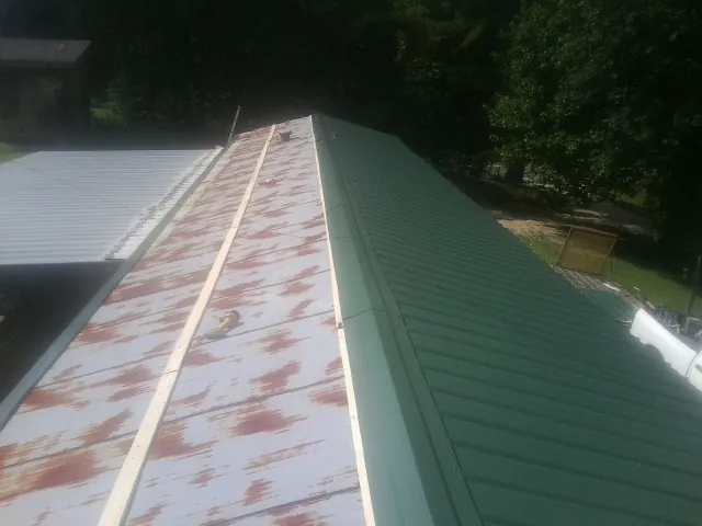 Old rusted panels beside newly installed green metal roofing — Wind Damage Roof Repair by Roofing Brothers in Glen Hope