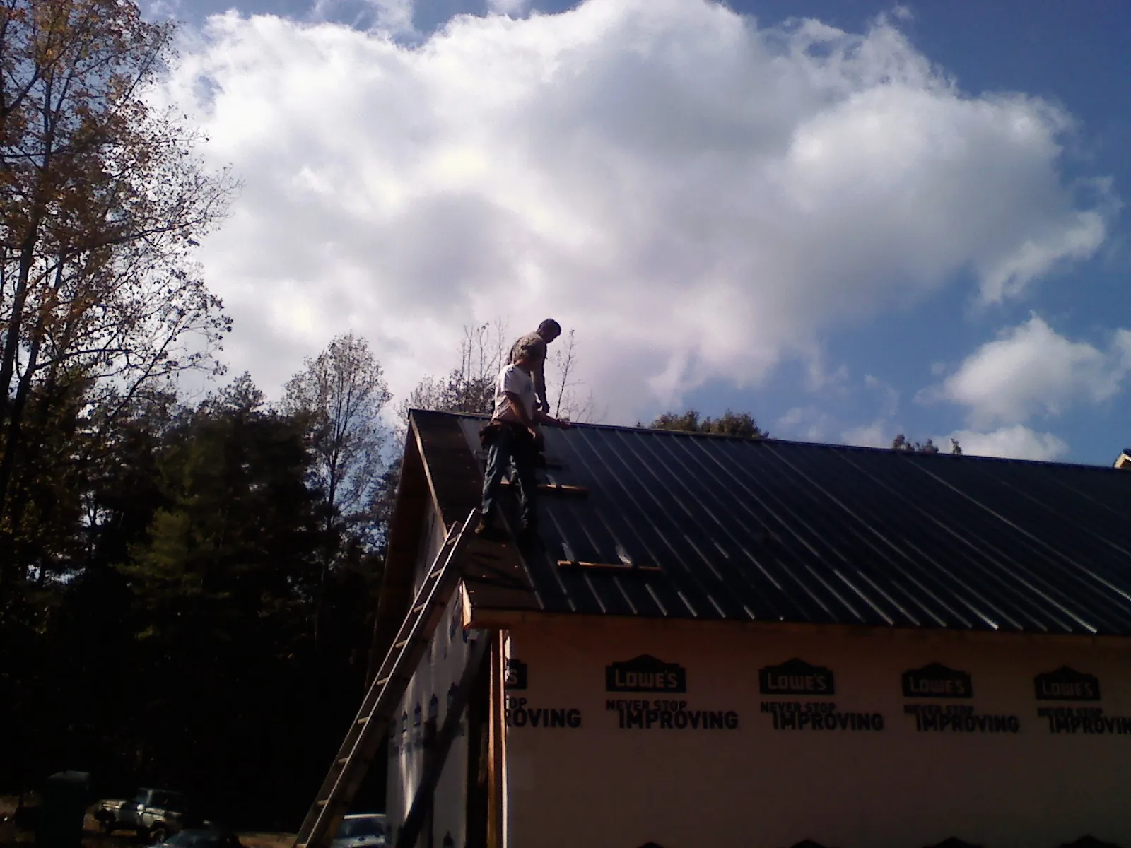 Roofer fastening dark metal panels high against a cloudy sky, from a Roof Inspection job in Glen Hope