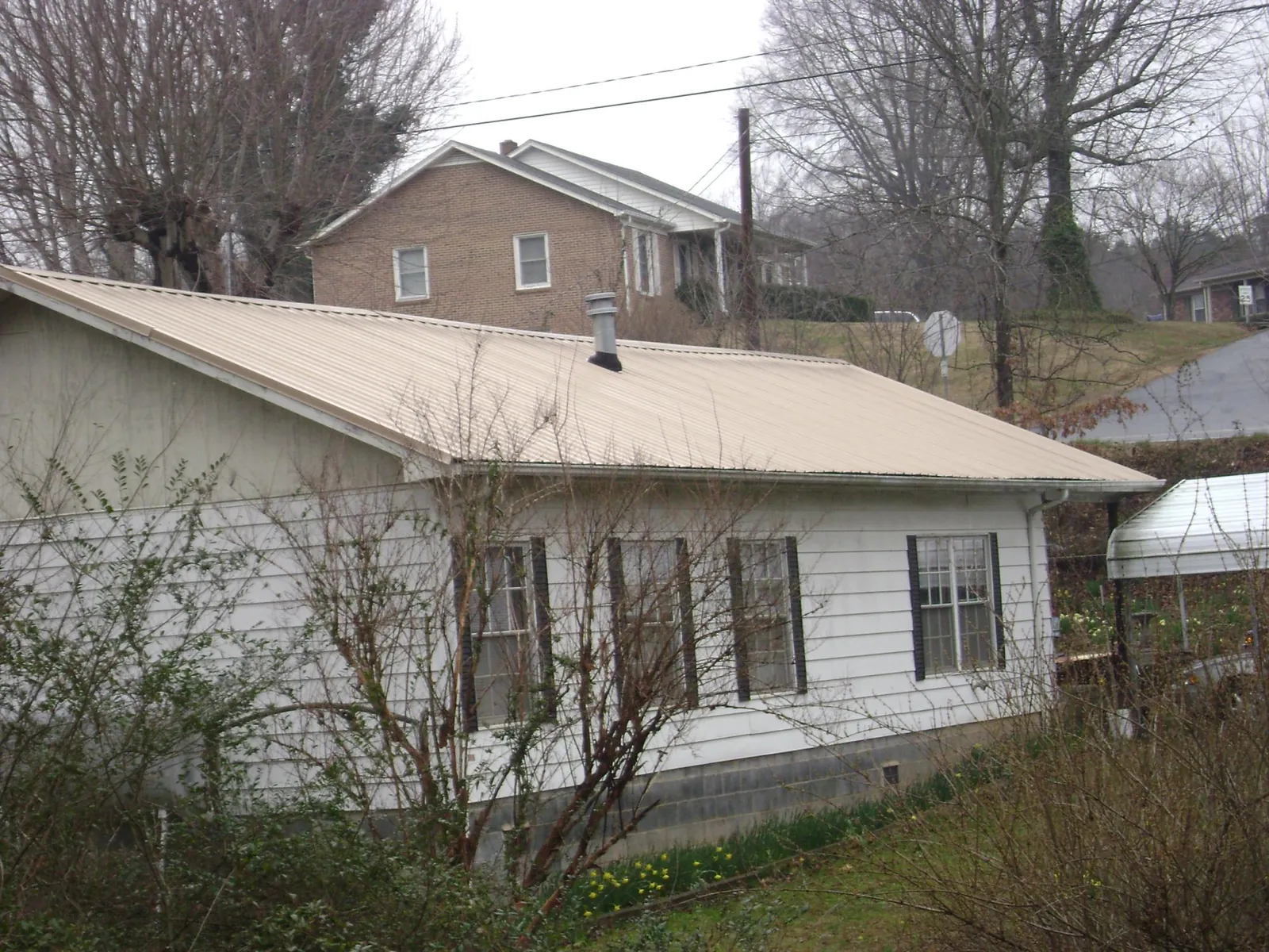 Tan metal roof on a white sided house set into a hillside — Commercial Roofing by Roofing Brothers in Glen Hope