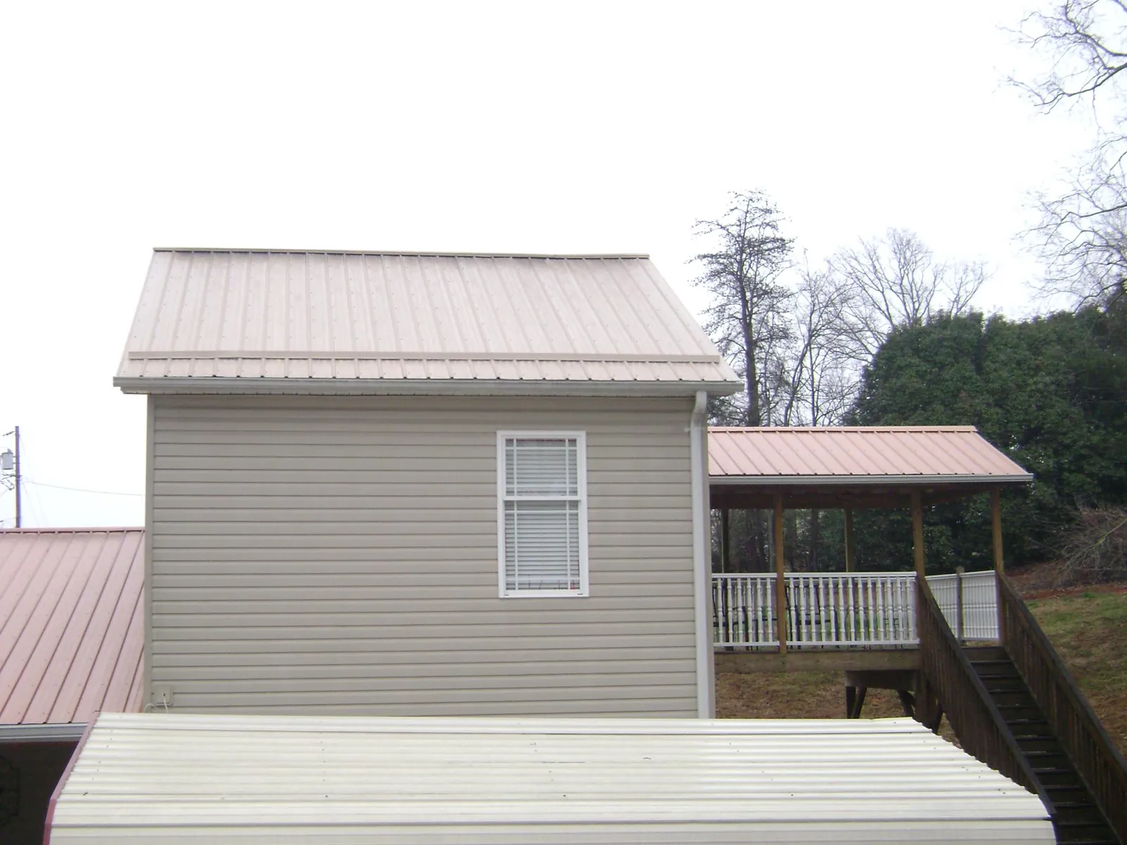 Tan metal roofs on a two story addition and attached porch, from a Roof Replacement job in Glen Hope